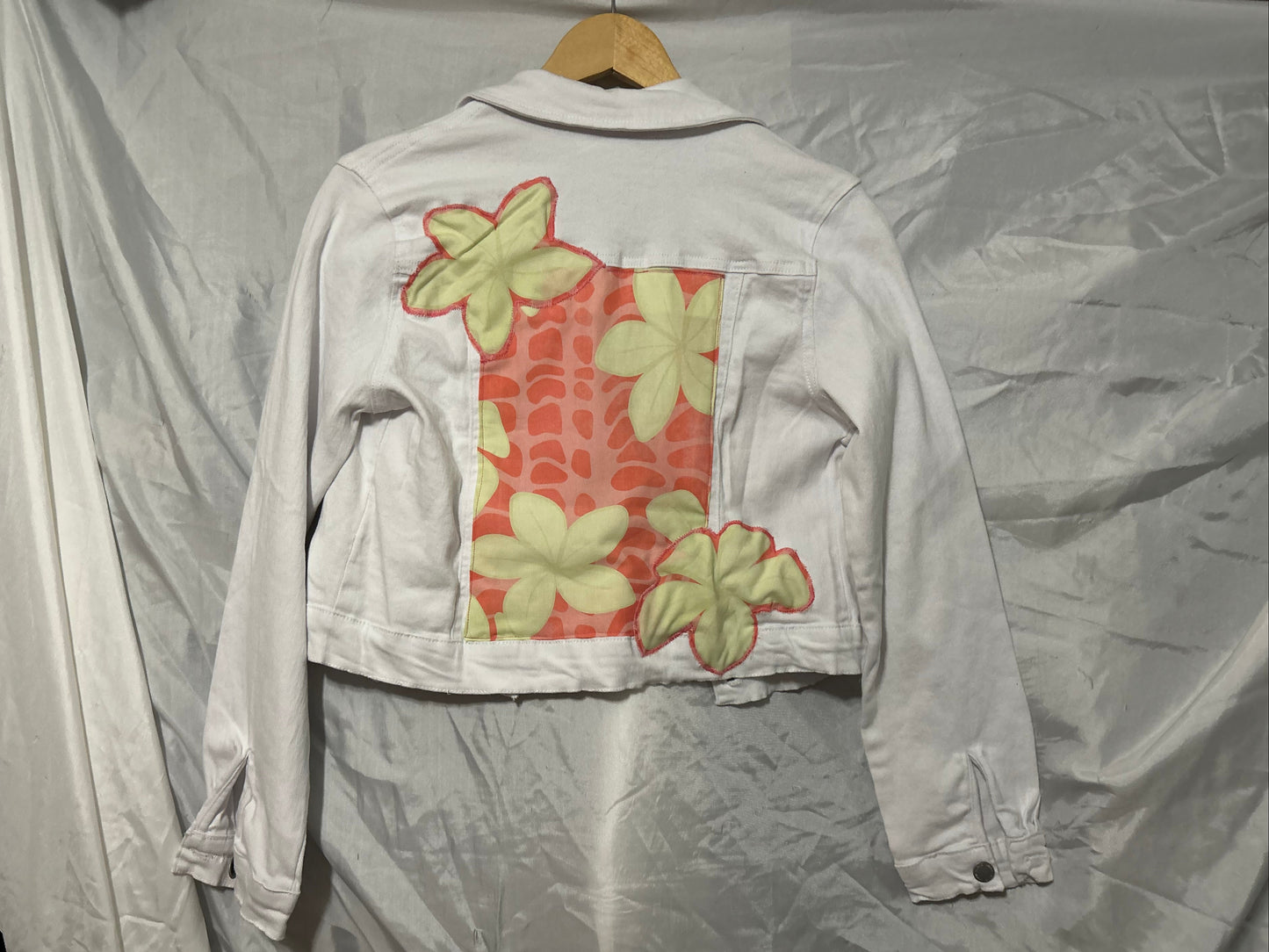 Light-colored jacket with floral patterns on a hanger against a plain background